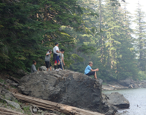 Natural Resources kids with walking sticks on top of big rock at the water